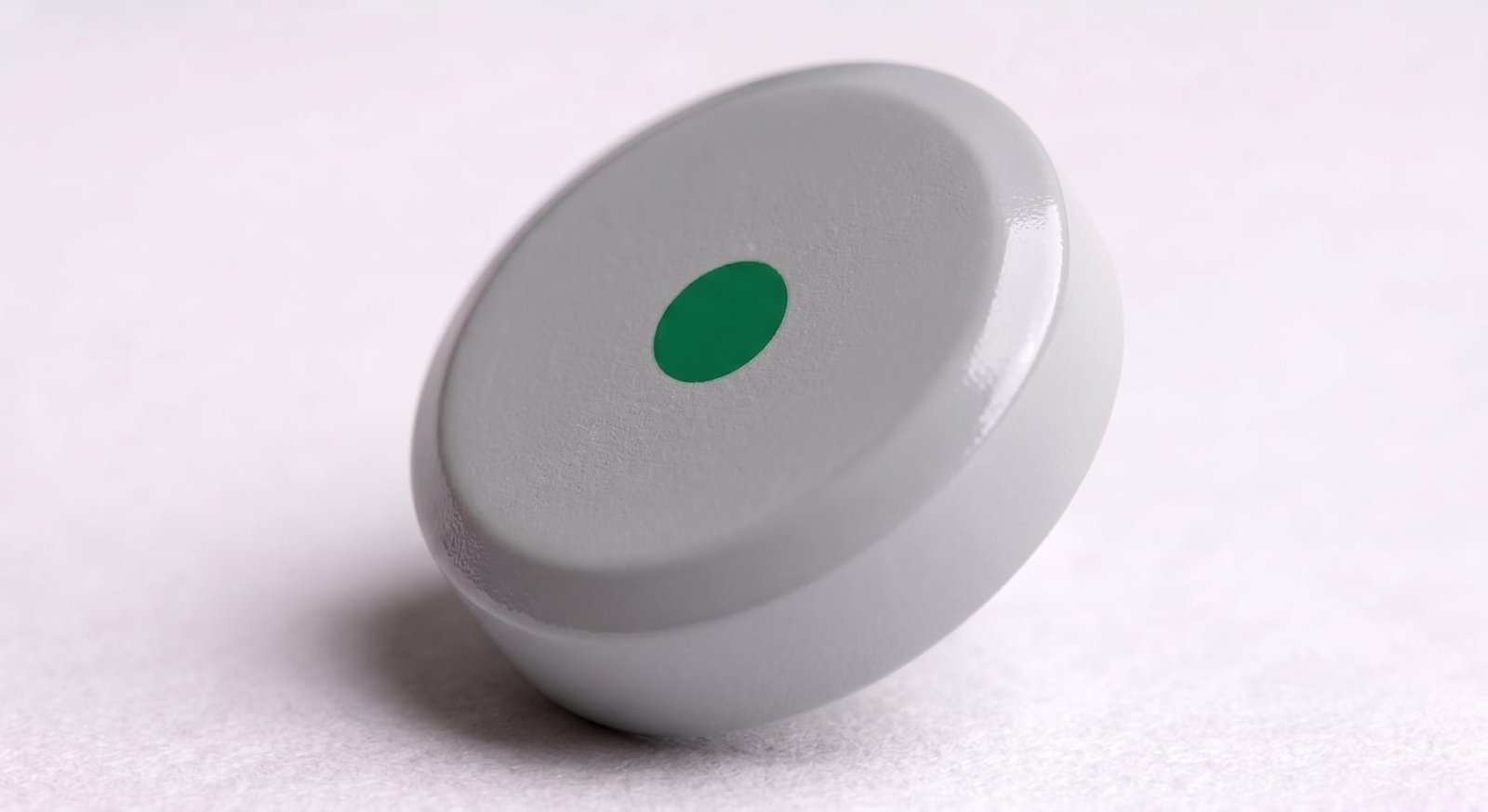 A smooth light-gray TABCOTE tablet with a beveled edge and a green dot printed on its face